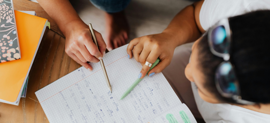 Student solving math sums on a notebook, with a teacher