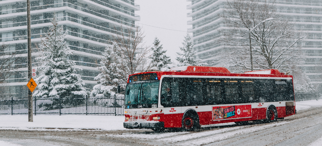 A red TTC bus driving through the snow